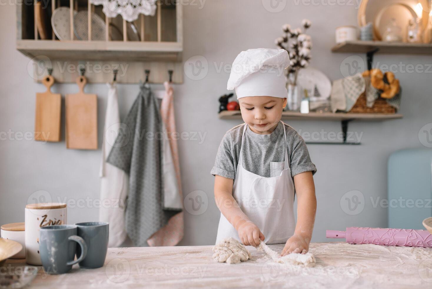 Young boy cute on the kitchen cook chef in white uniform and hat near table. homemade gingerbread. the boy cooked the chocolate cookies. photo