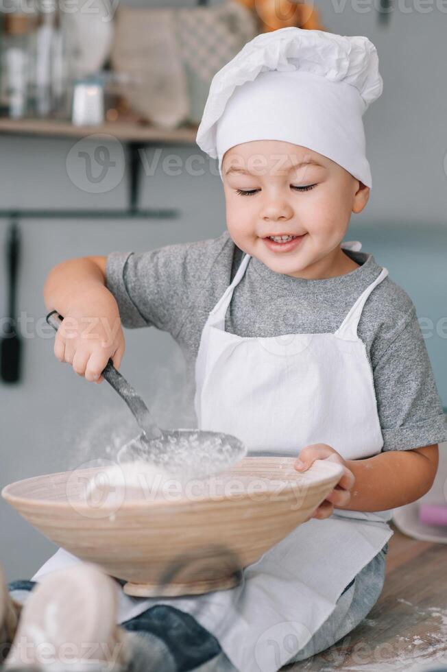 Young boy cute on the kitchen cook chef in white uniform and hat near table. homemade gingerbread. the boy cooked the chocolate cookies photo