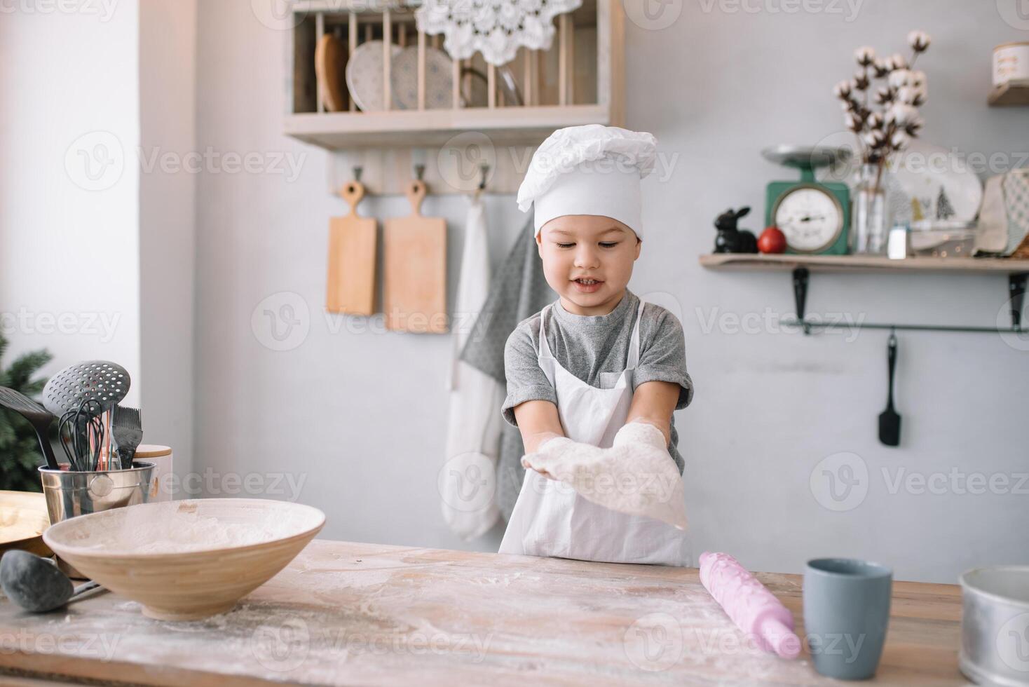 joven chico linda en el cocina cocinar cocinero en blanco uniforme y sombrero cerca mesa. hecho en casa pan de jengibre. el chico cocido el chocolate galletas. foto