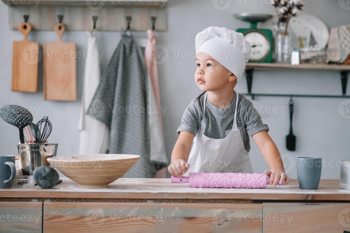 joven chico linda en el cocina cocinar cocinero en blanco uniforme y sombrero cerca mesa. hecho en casa pan de jengibre. el chico cocido el chocolate galletas foto