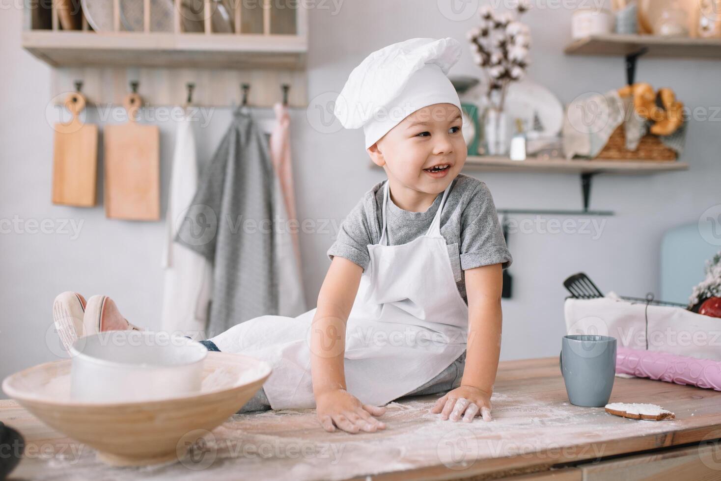 Young boy cute on the kitchen cook chef in white uniform and hat near table. homemade gingerbread. the boy cooked the chocolate cookies. photo