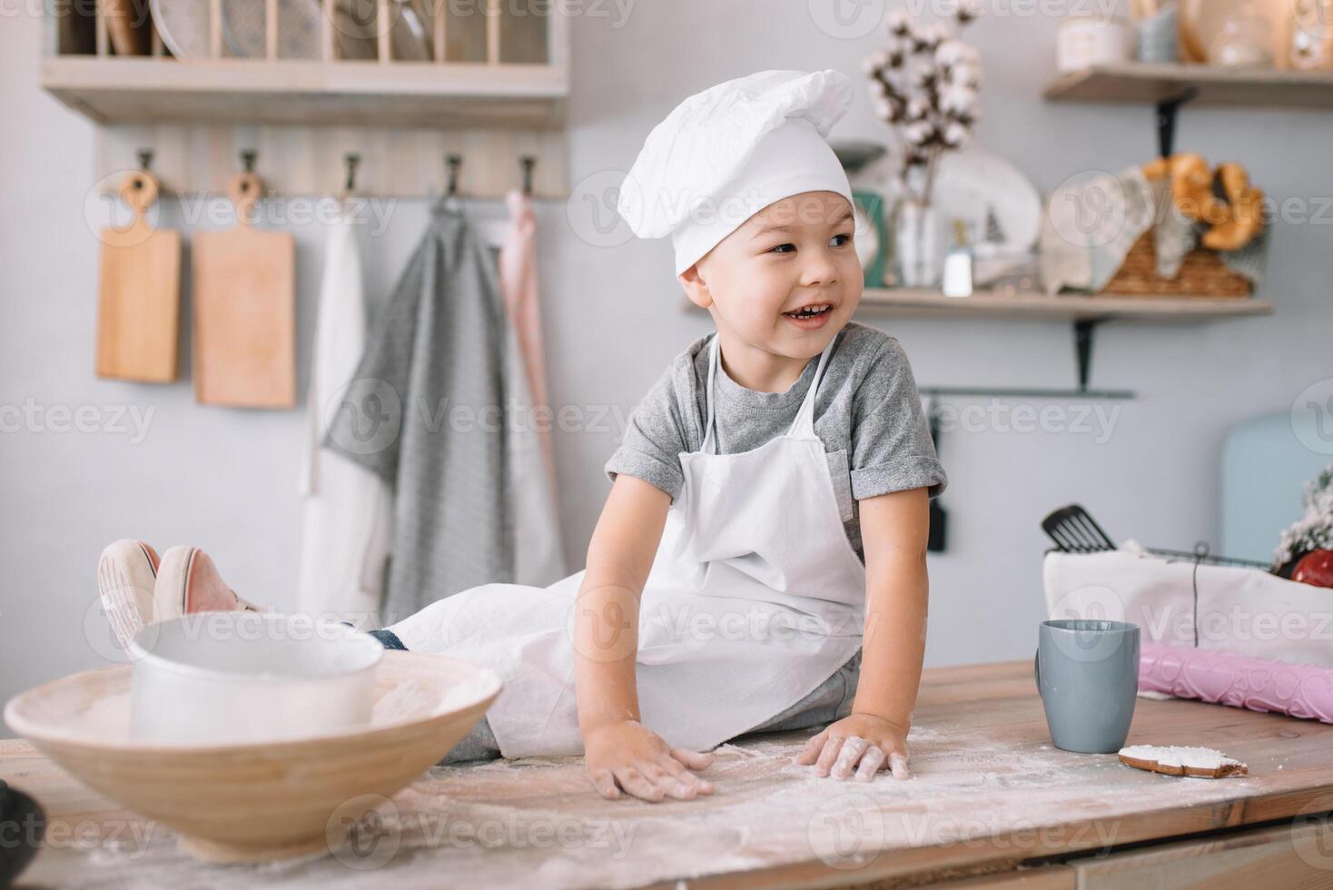 joven chico linda en el cocina cocinar cocinero en blanco uniforme y sombrero cerca mesa. hecho en casa pan de jengibre. el chico cocido el chocolate galletas. foto