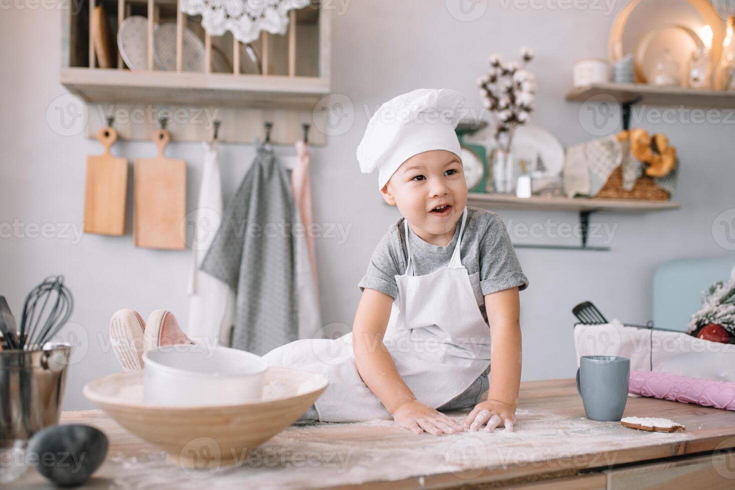 joven chico linda en el cocina cocinar cocinero en blanco uniforme y sombrero cerca mesa. hecho en casa pan de jengibre. el chico cocido el chocolate galletas. foto