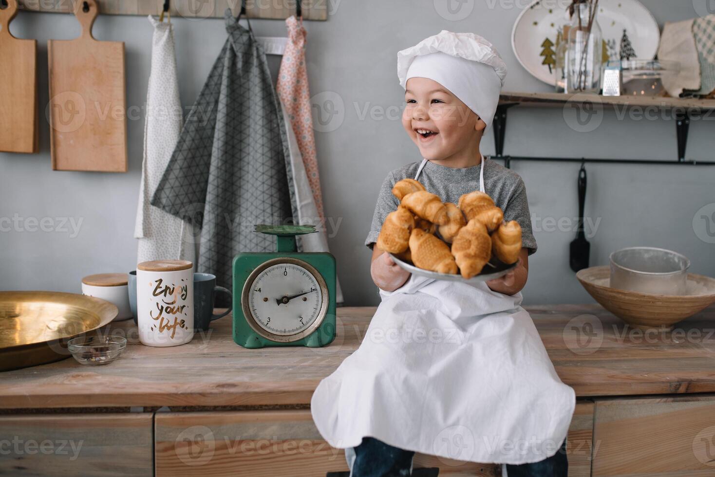 joven chico linda en el cocina cocinar cocinero en blanco uniforme y sombrero cerca mesa. hecho en casa pan de jengibre. el chico cocido el chocolate galletas. foto