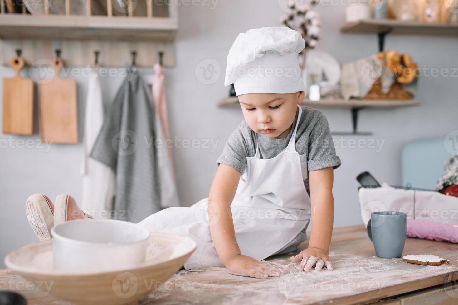 joven chico linda en el cocina cocinar cocinero en blanco uniforme y sombrero cerca mesa. hecho en casa pan de jengibre. el chico cocido el chocolate galletas. foto