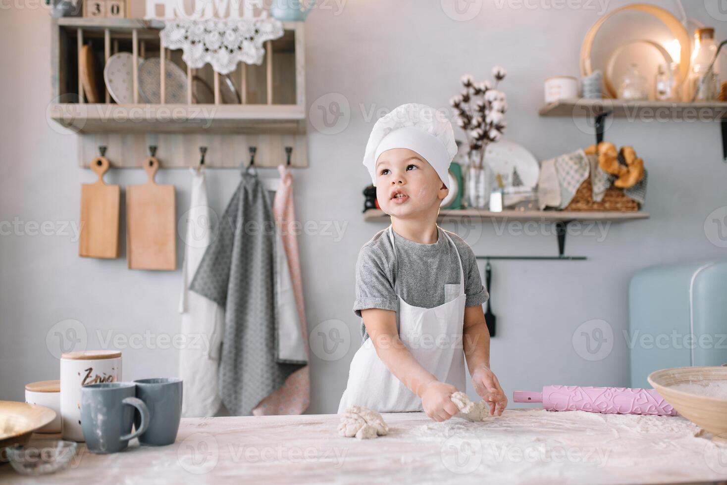 Young boy cute on the kitchen cook chef in white uniform and hat near table. homemade gingerbread. the boy cooked the chocolate cookies. photo