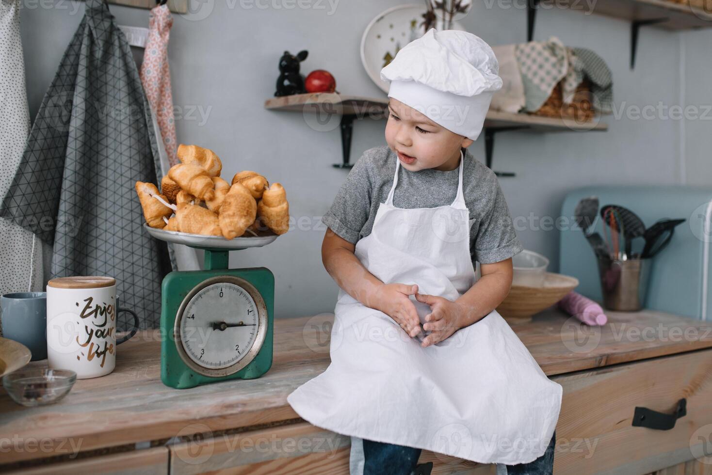 joven chico linda en el cocina cocinar cocinero en blanco uniforme y sombrero cerca mesa. hecho en casa pan de jengibre. el chico cocido el chocolate galletas. foto