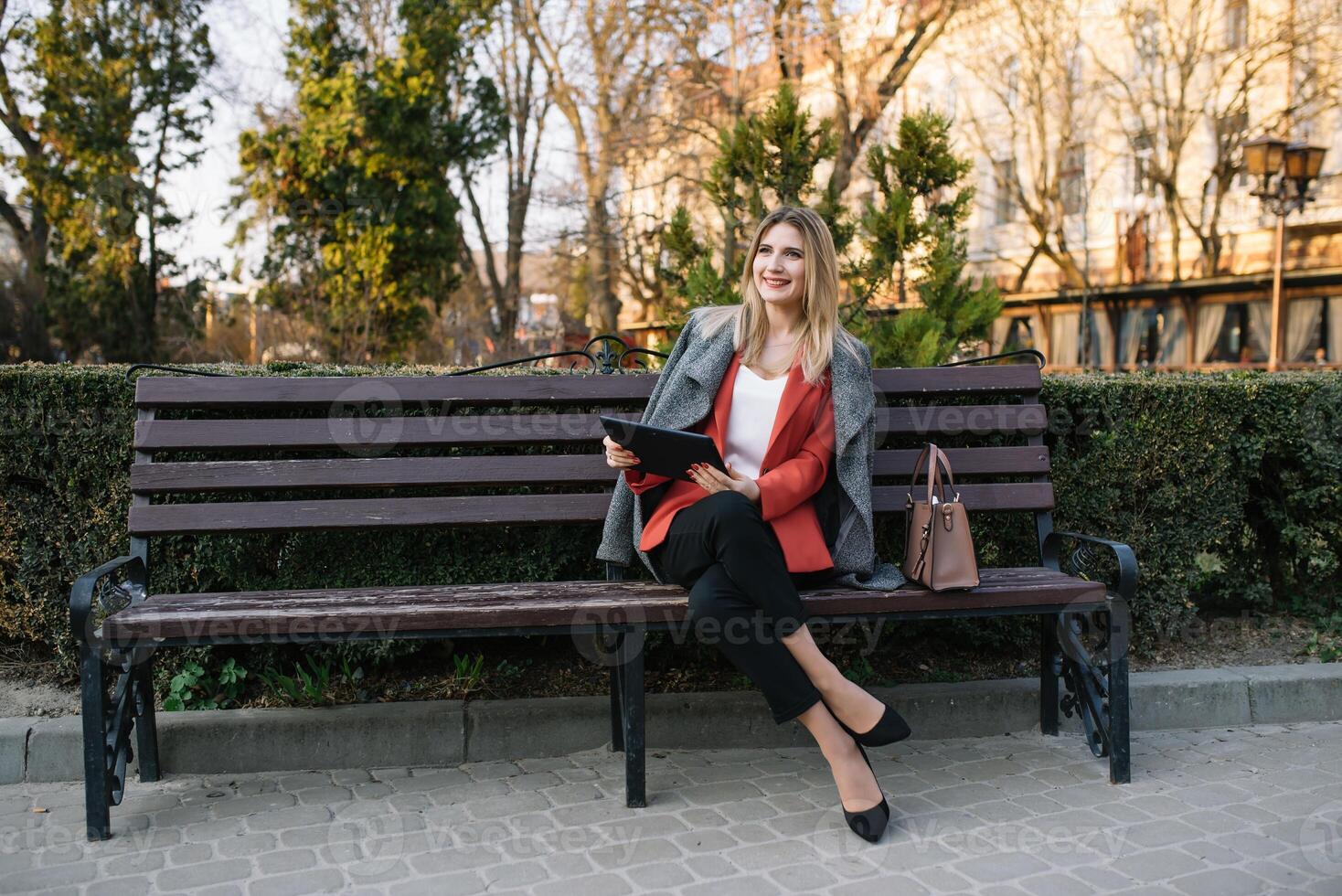 Beautiful woman using tablet computer on an urban bench. Businesswoman wearing suit with trousers and tie, afro hairstyle photo