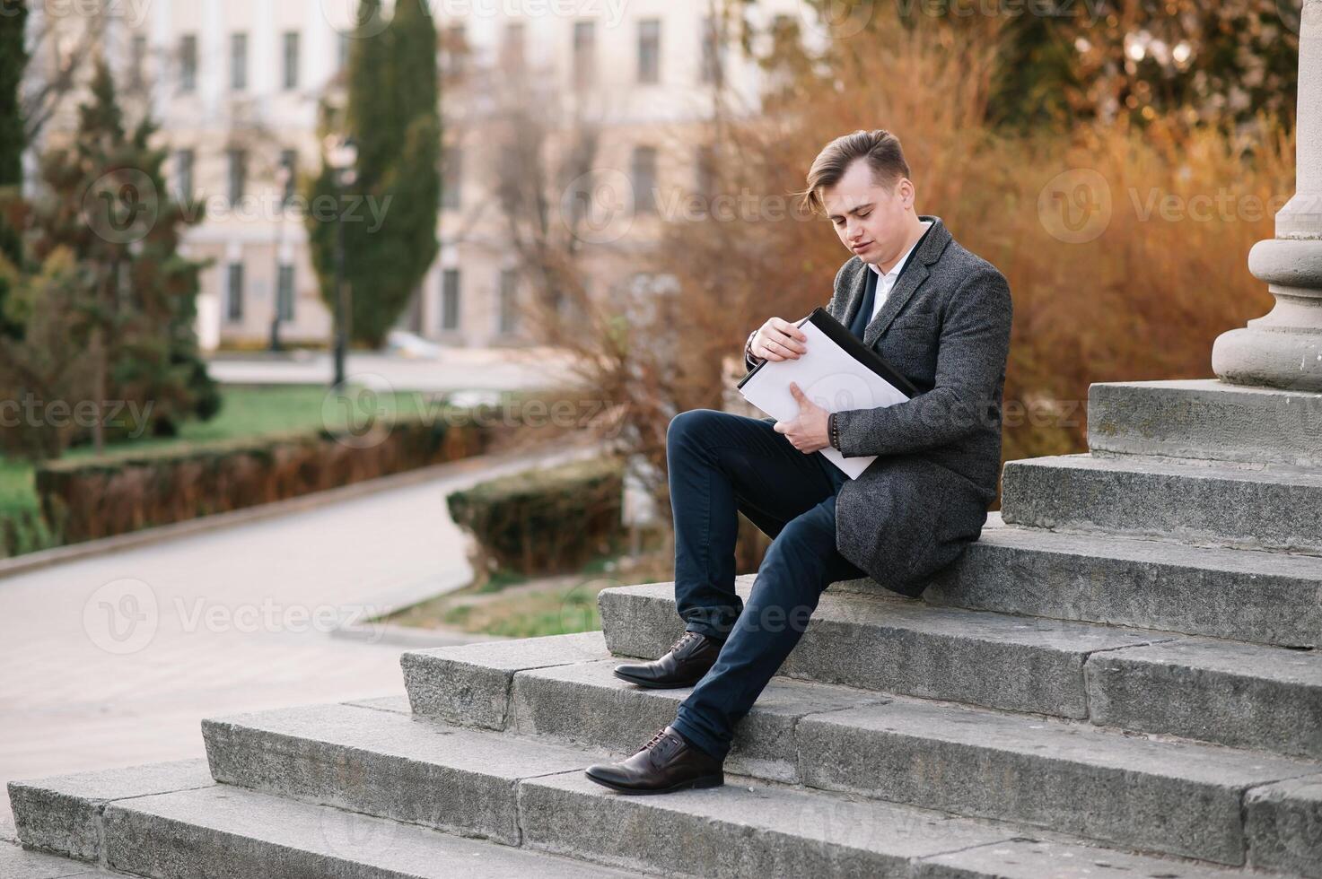 Handsome young businessman working with documents sitting on the stairs outdoor photo