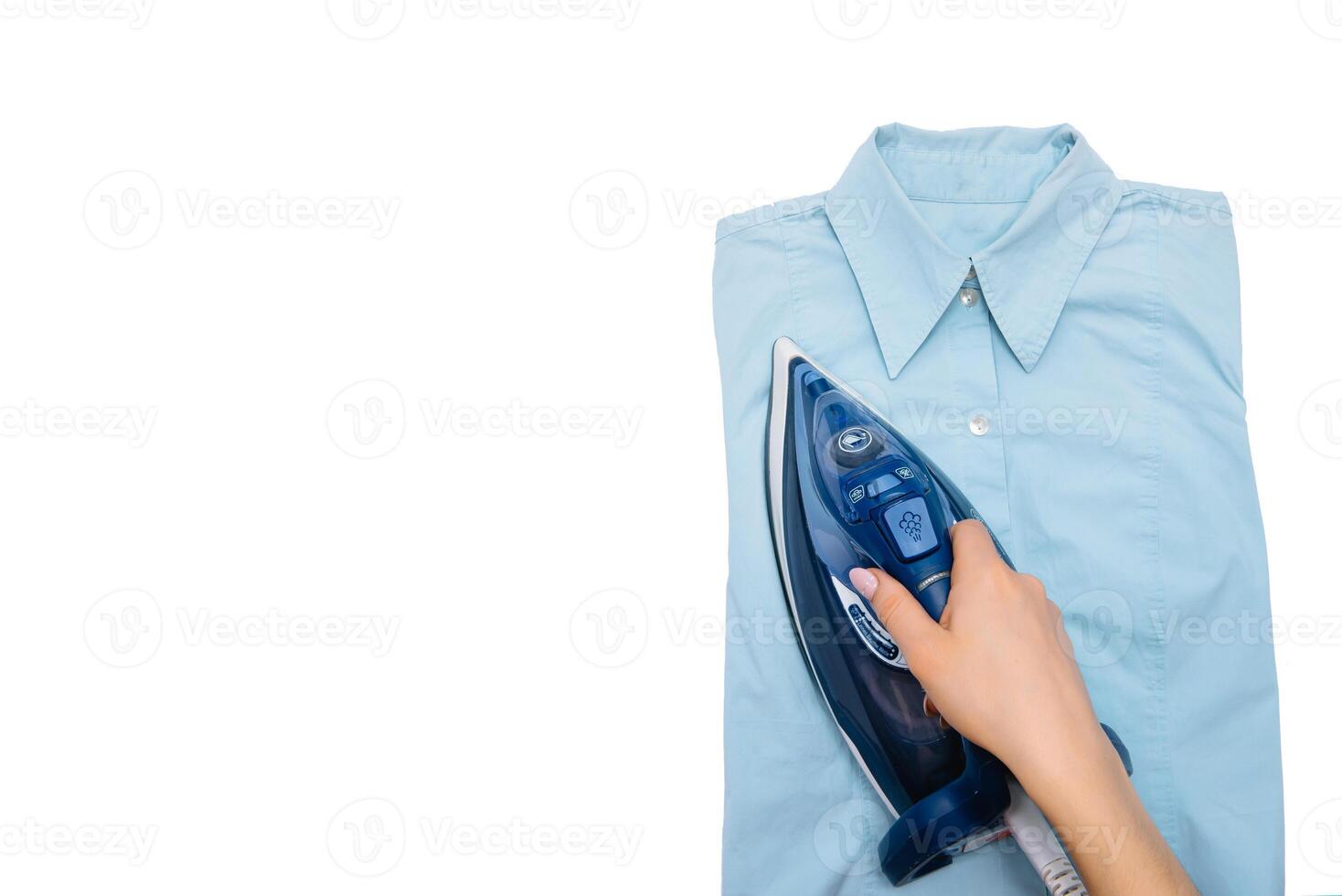 Female hand ironing clothes top view isolated on white background. Young woman with iron ironing man's shirt seen from above during housework. Blue iron on white table photo