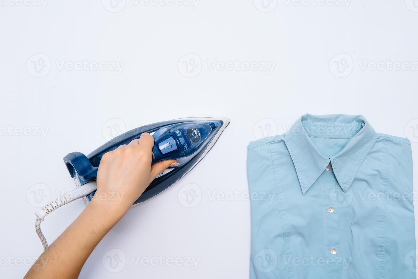 Female hand ironing clothes top view isolated on white background. Young woman with iron ironing man's shirt seen from above during housework. Blue iron on white table photo