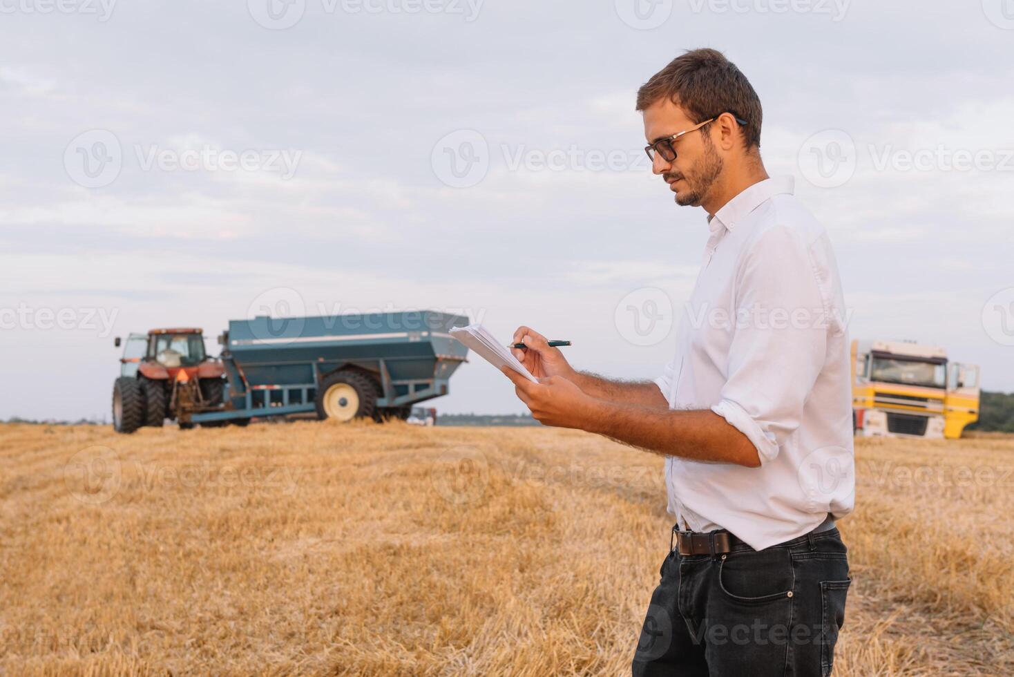 Young attractive farmer with laptop standing in wheat field with combine harvester in background. photo