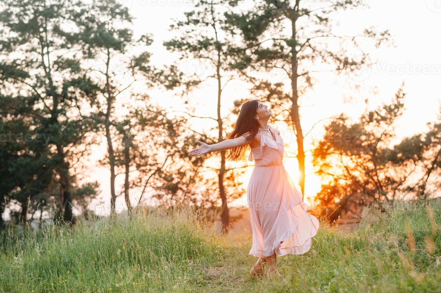 belleza joven niña al aire libre disfrutando naturaleza. Moda joven mujer en rosado vestir y elegante sombrero en prado con Copiar espacio. foto