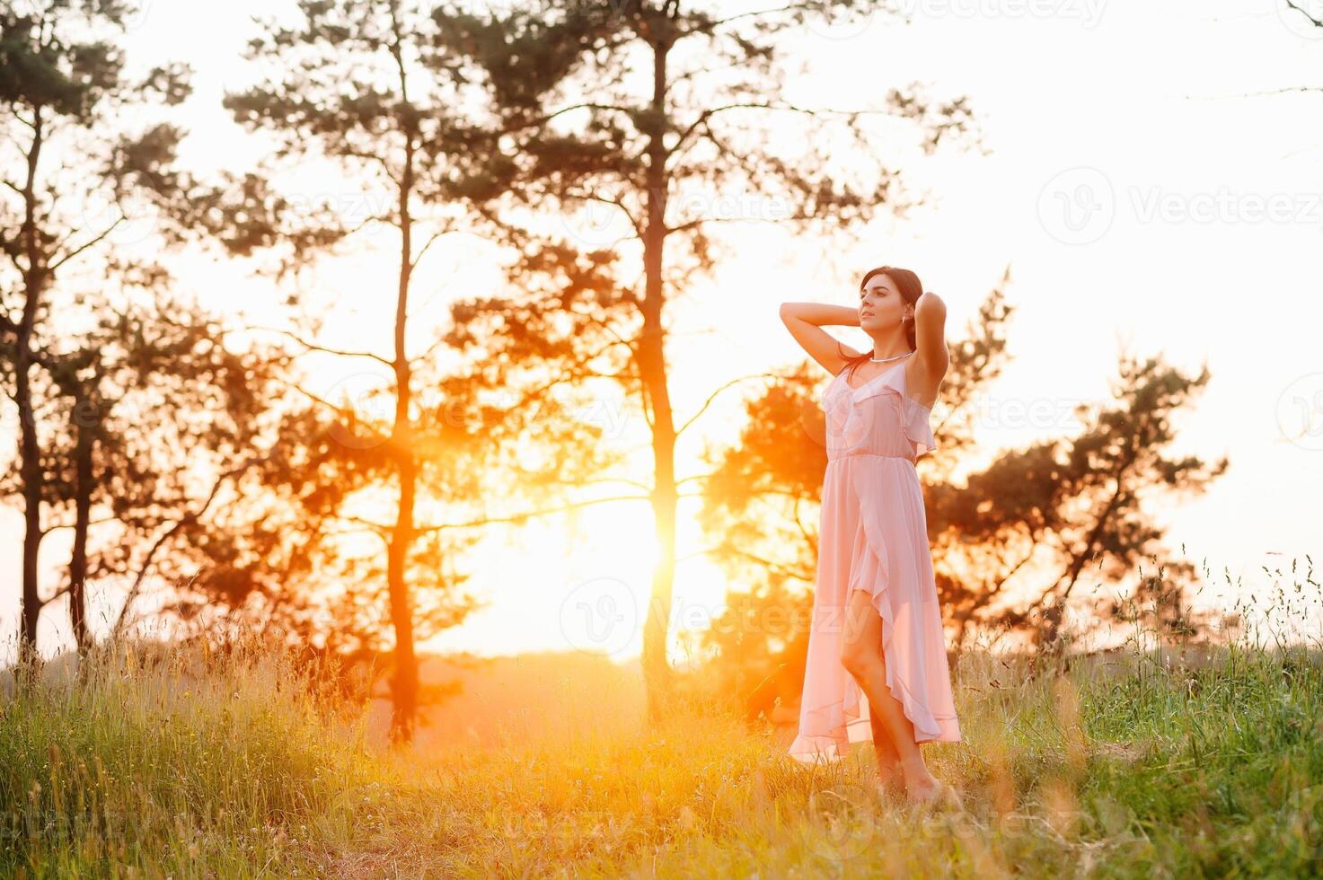 belleza joven niña al aire libre disfrutando naturaleza. Moda joven mujer en rosado vestir y elegante sombrero en prado con Copiar espacio. foto