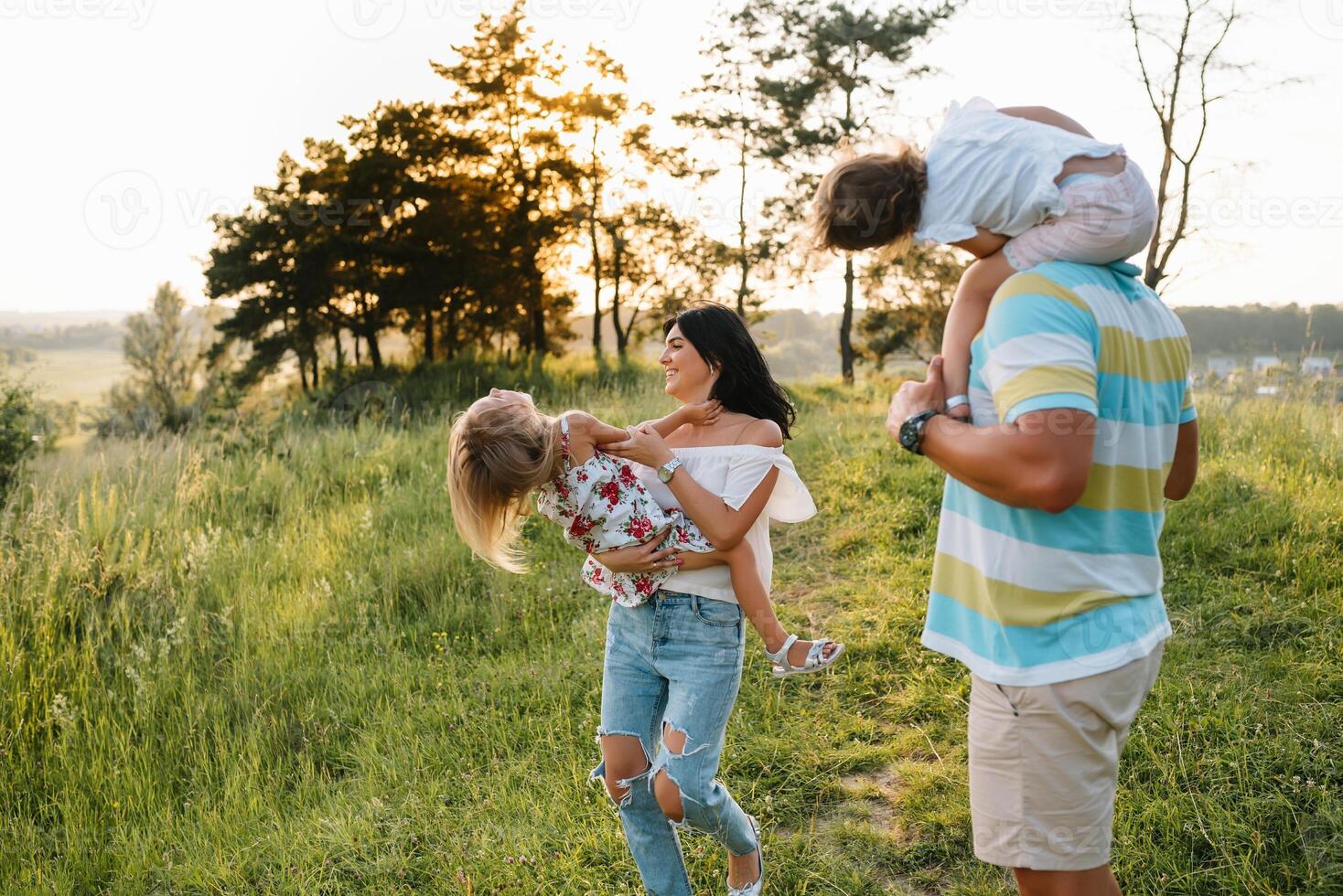 color foto de sonriente joven padres y dos niños, descanso y tener divertido en naturaleza. amar, familia y contento infancia estilo de vida concepto.