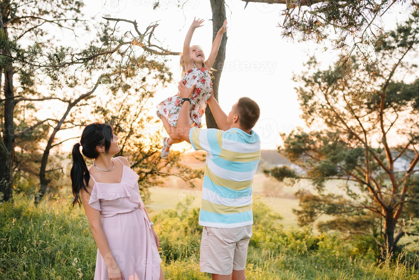 Happy family walking in the park. Mom, dad and daughter walk outdoors, parents holding the baby girl's hands. Childhood, parenthood, family bonds, marriage concept photo