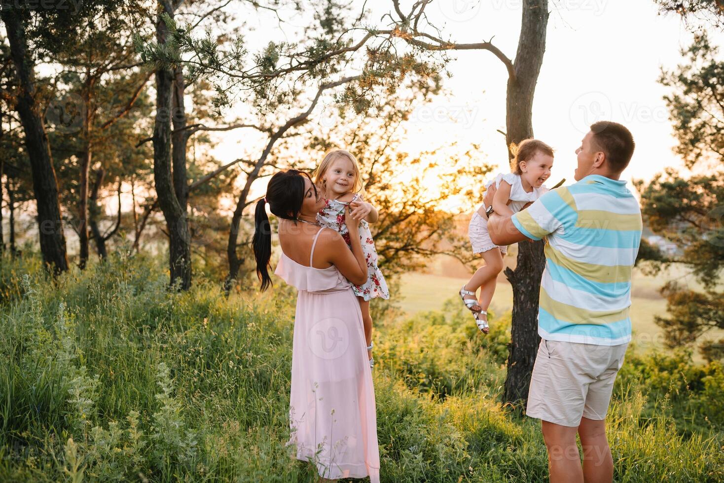 color foto de sonriente joven padres y dos niños, descanso y tener divertido en naturaleza. amar, familia y contento infancia estilo de vida concepto