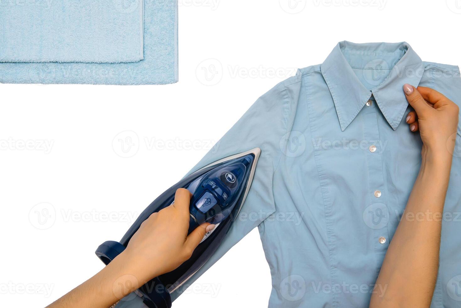 Female hand ironing clothes top view isolated on white background. Young woman with iron ironing man's shirt seen from above during housework. Blue iron on white table photo