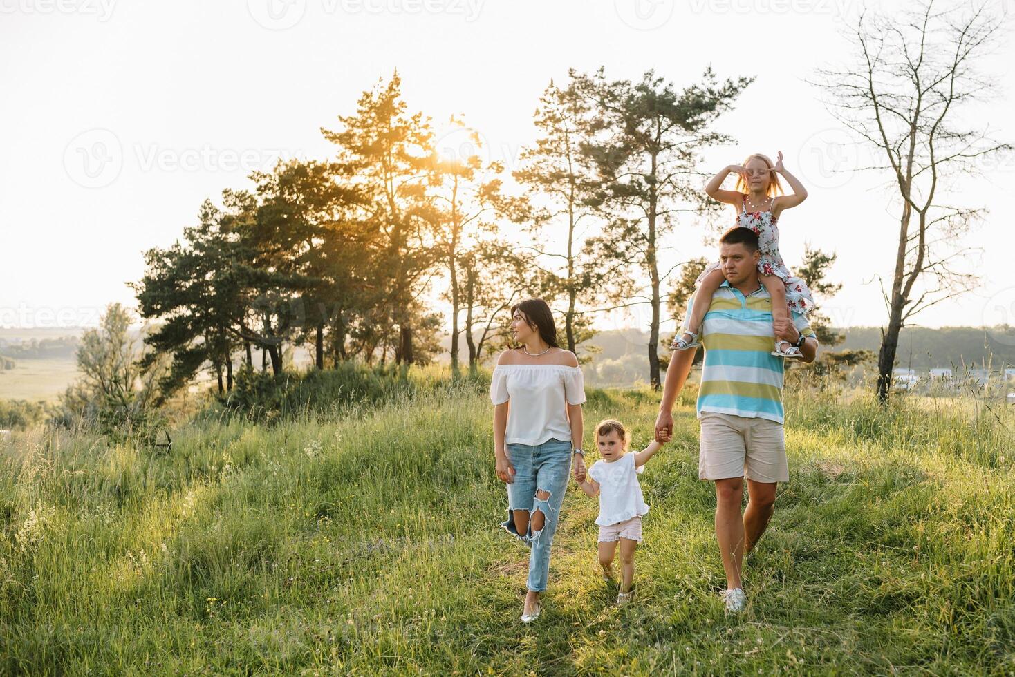 color foto de sonriente joven padres y dos niños, descanso y tener divertido en naturaleza. amar, familia y contento infancia estilo de vida concepto.