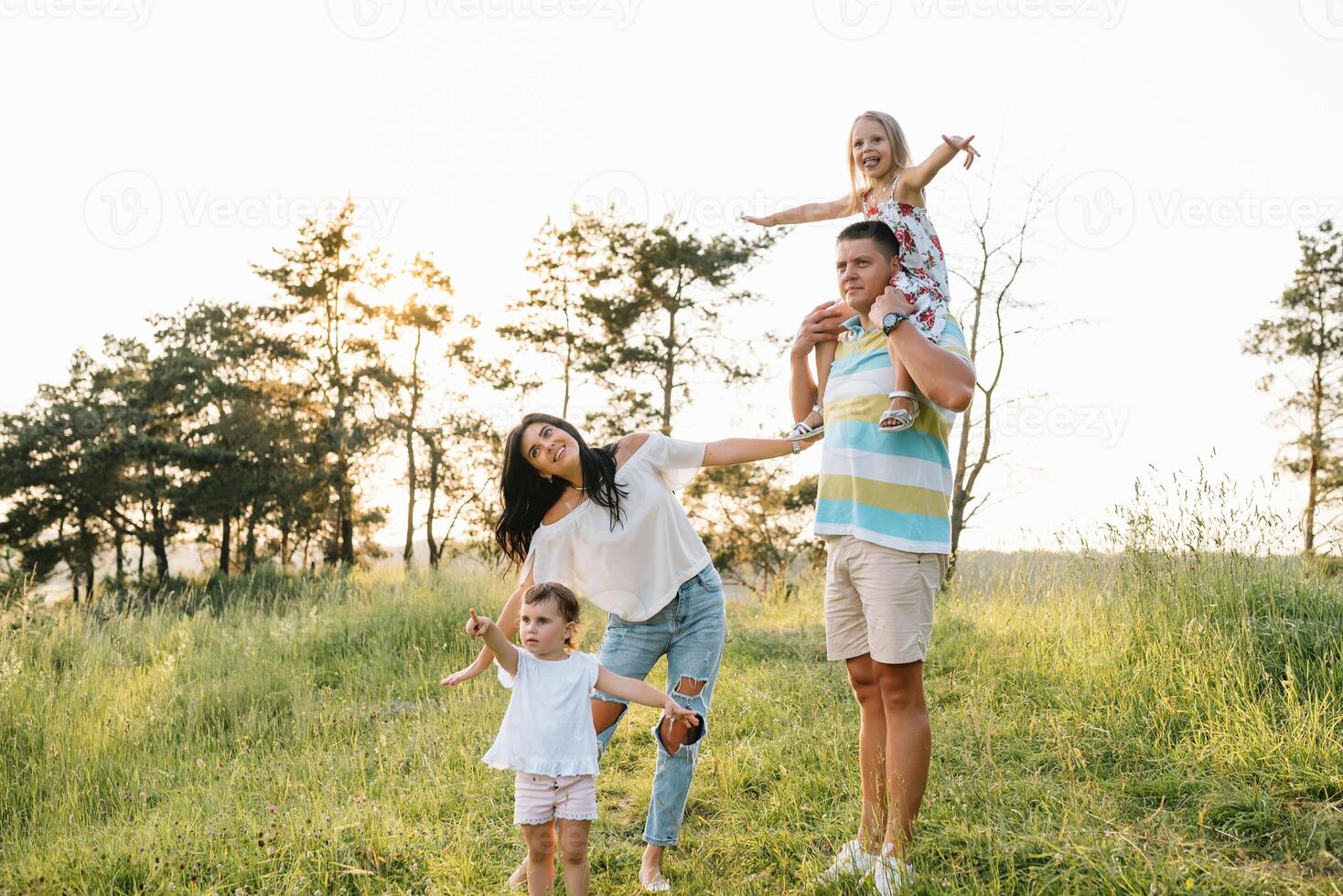 Color photo of smiling young parents and two children, rest and have fun in nature. Love, family and happy childhood lifestyle concept.