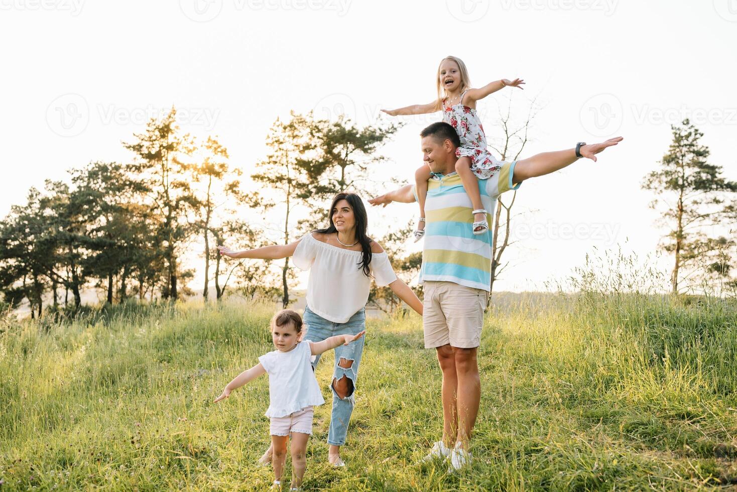 color foto de sonriente joven padres y dos niños, descanso y tener divertido en naturaleza. amar, familia y contento infancia estilo de vida concepto.