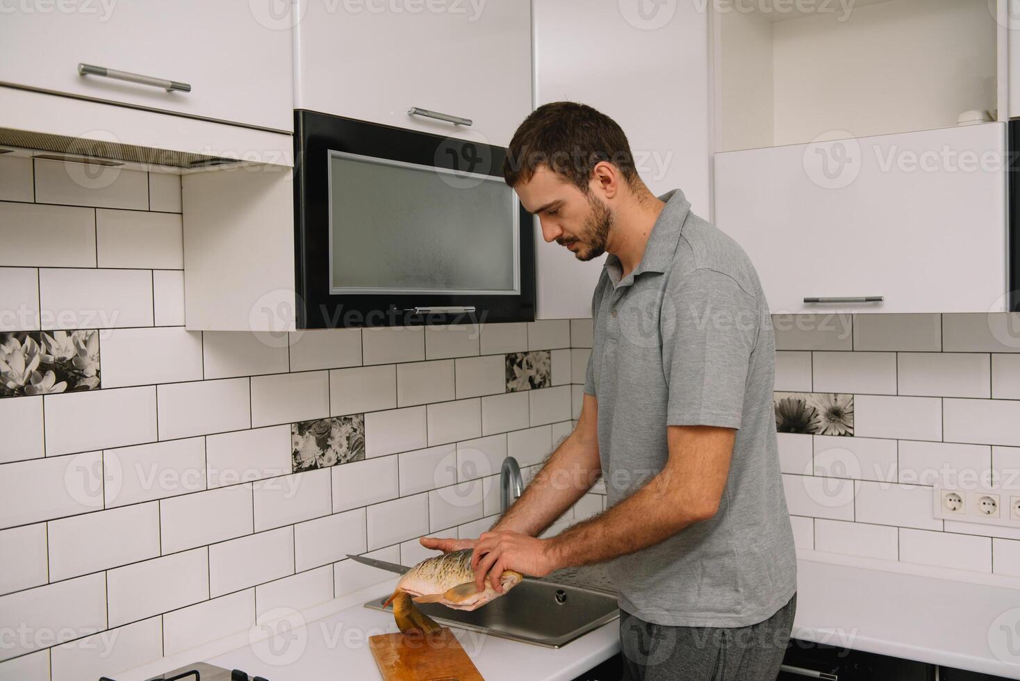 Man cutting fresh fish in kitchen in home. Man butchering fish for cook. photo