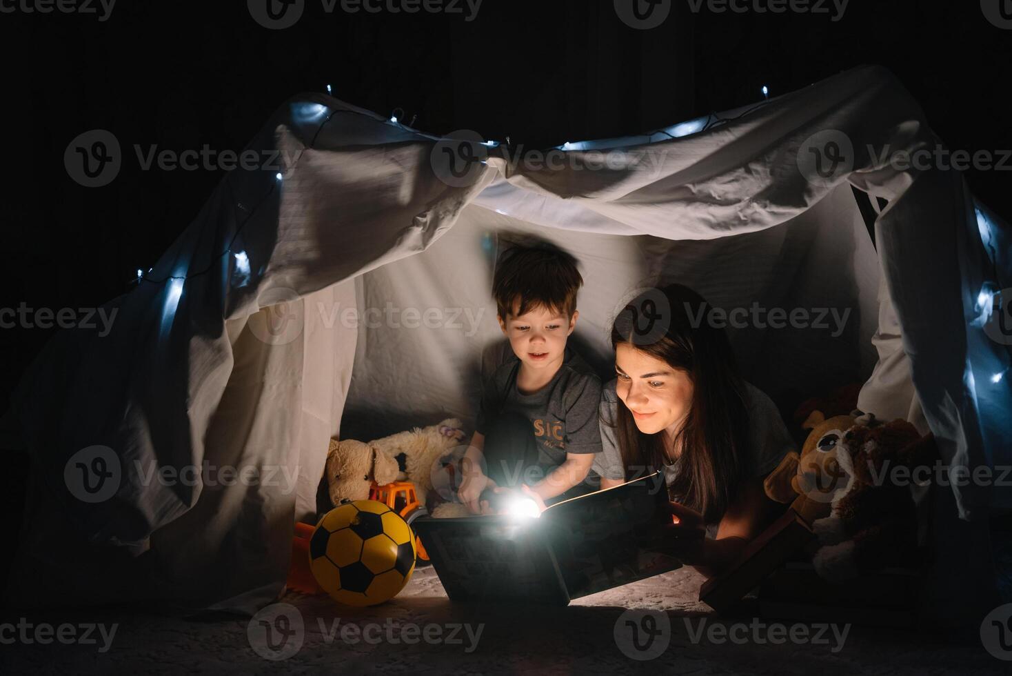happy family mother and child son reading a book with a flashlight in a tent at home. family concept. photo