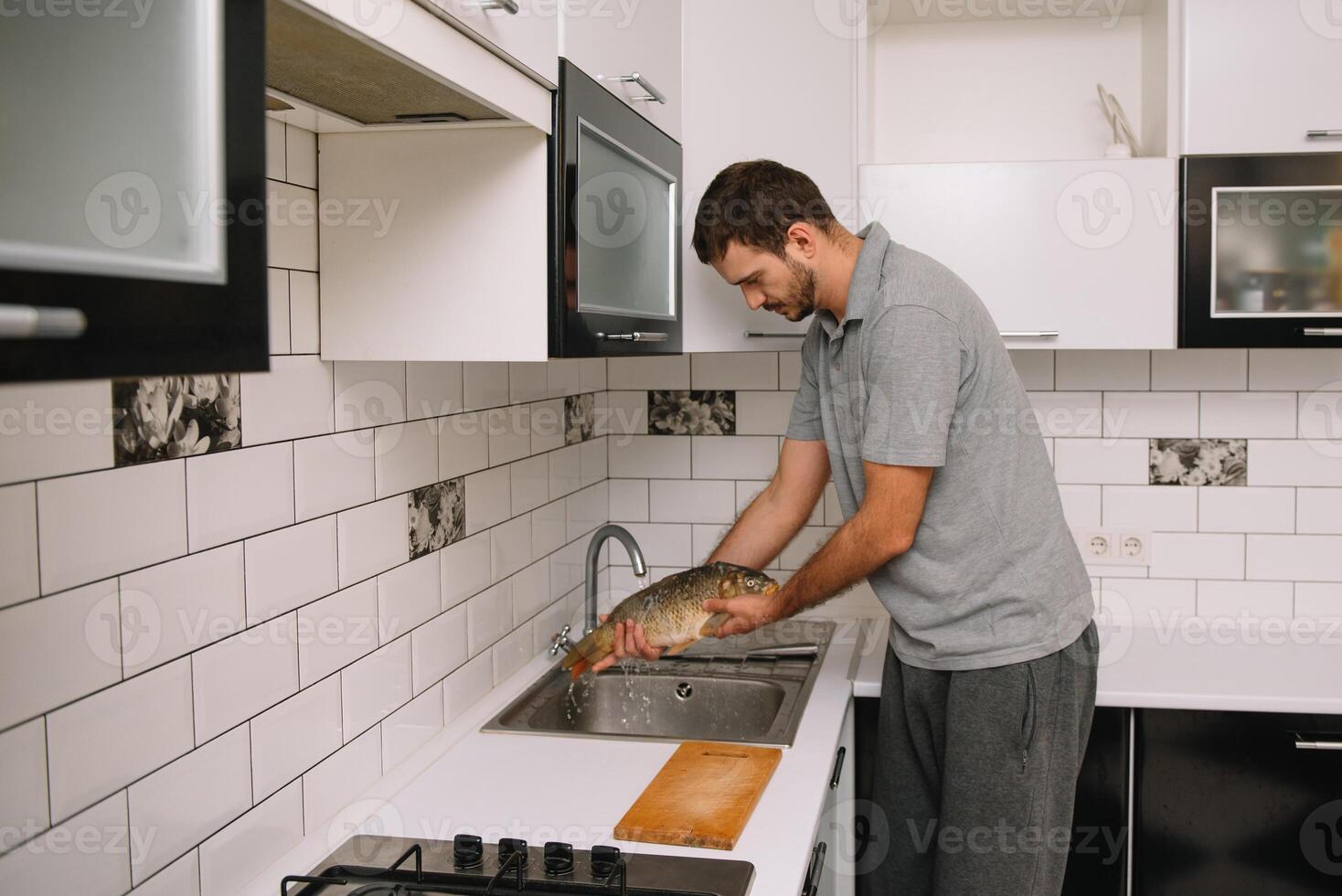 Man cutting fresh fish in kitchen in home. Man butchering fish for cook. photo