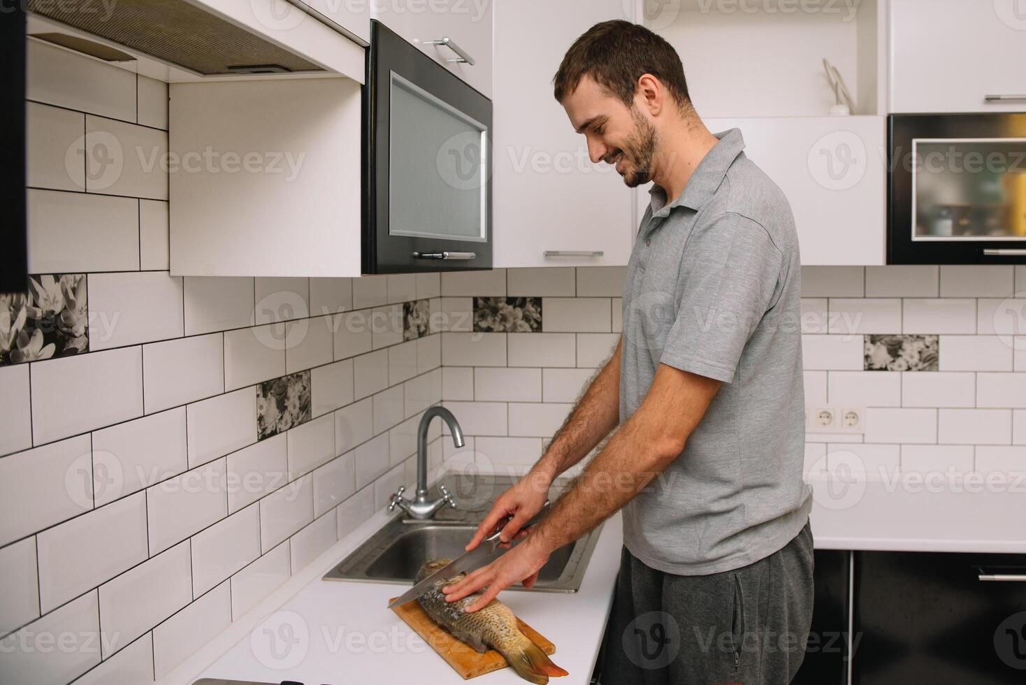 Man cutting fresh fish in kitchen in home. Man butchering fish for cook. photo