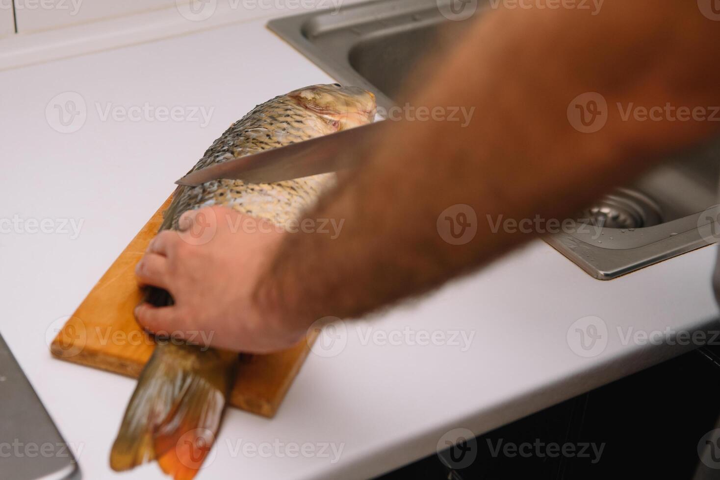 Man cutting fresh fish in kitchen in home. Man butchering fish for cook. photo