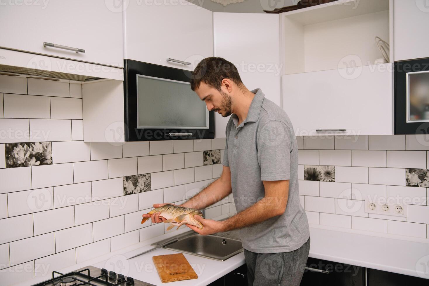 Man cutting fresh fish in kitchen in home. Man butchering fish for cook. photo