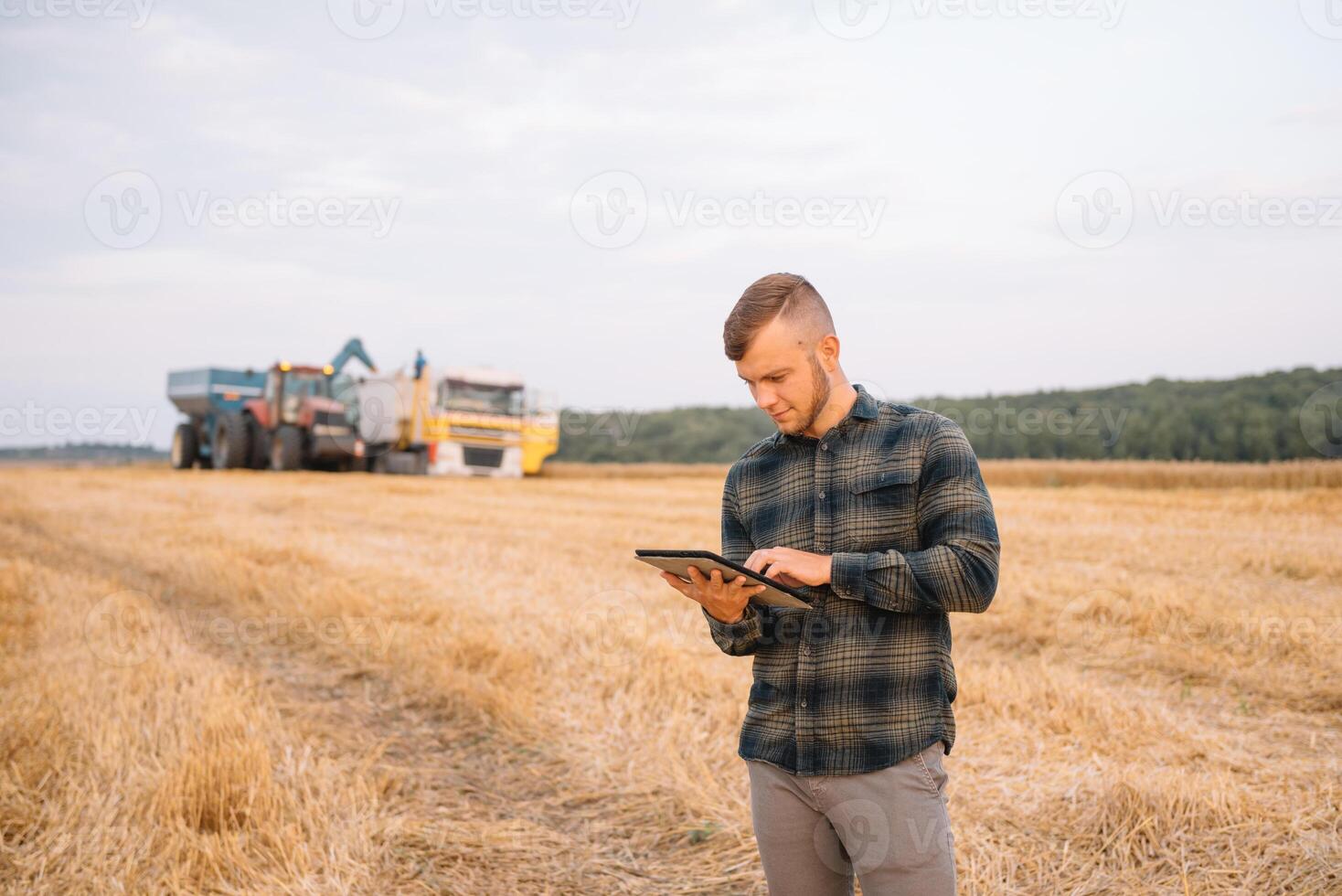 Young attractive farmer with laptop standing in wheat field with combine harvester in background. photo