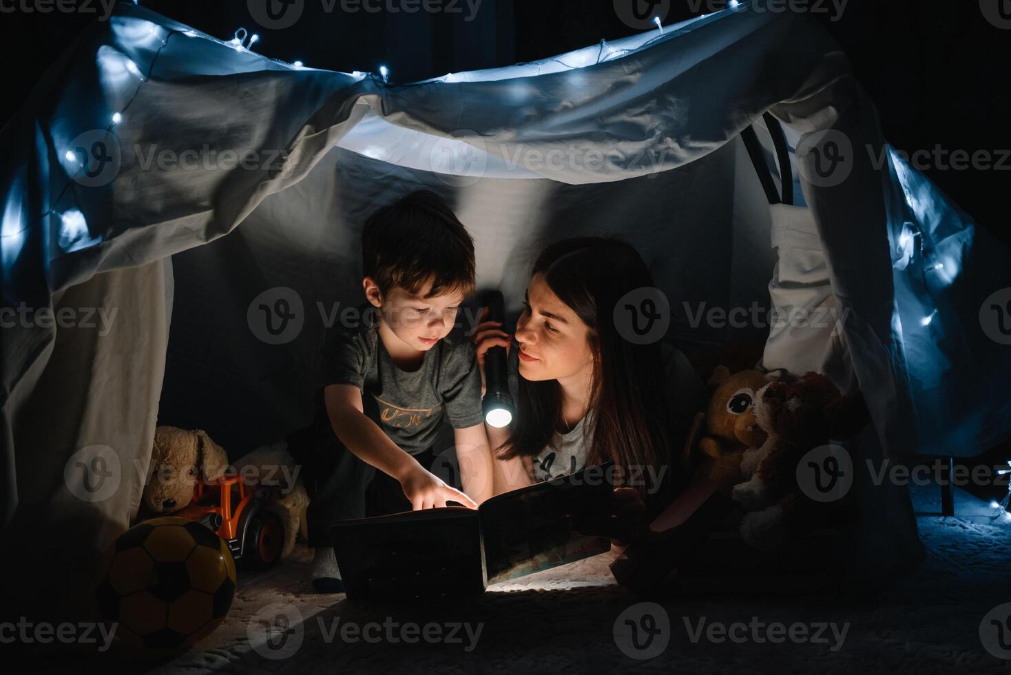 contento familia madre y niño hijo leyendo un libro con un Linterna en un tienda a hogar. familia concepto. foto