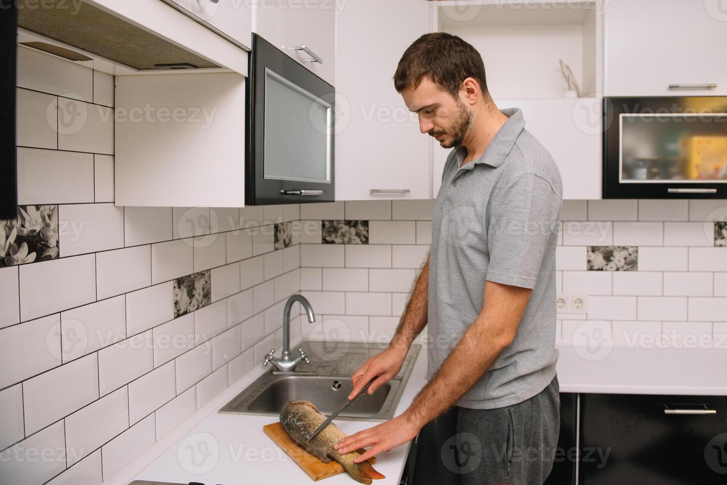 Man cutting fresh fish in kitchen in home. Man butchering fish for cook. photo