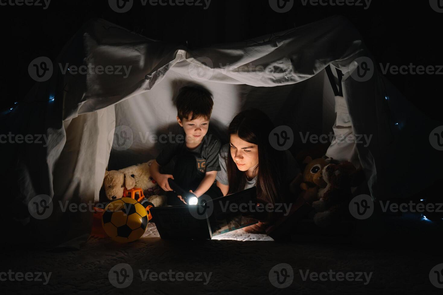 contento familia madre y niño hijo leyendo un libro con un Linterna en un tienda a hogar. familia concepto foto