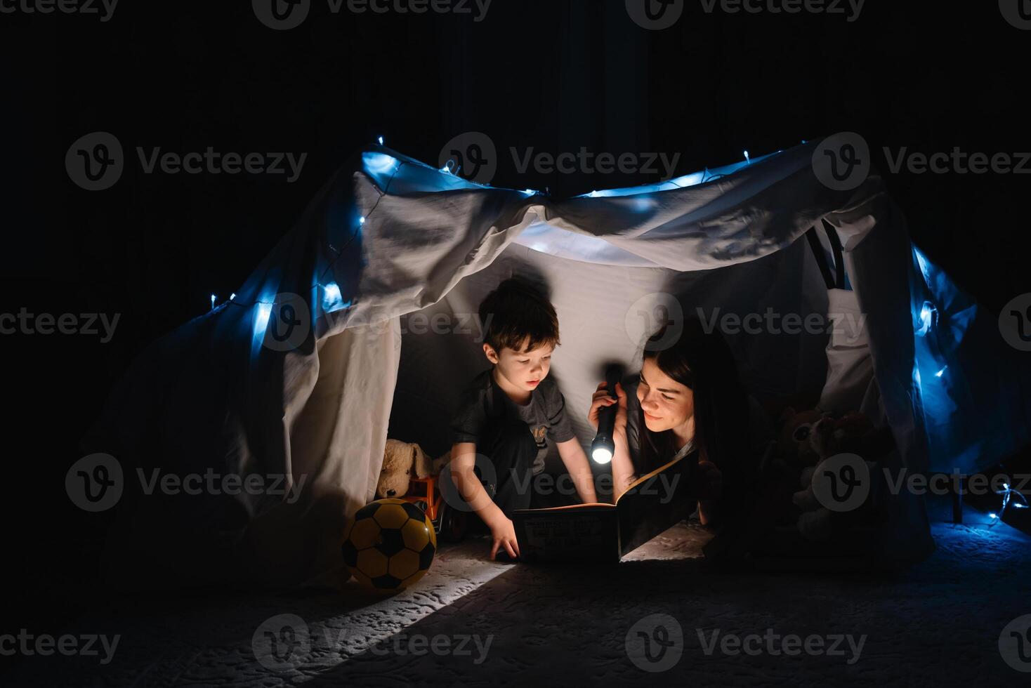 happy family mother and child son reading a book with a flashlight in a tent at home. family concept. photo