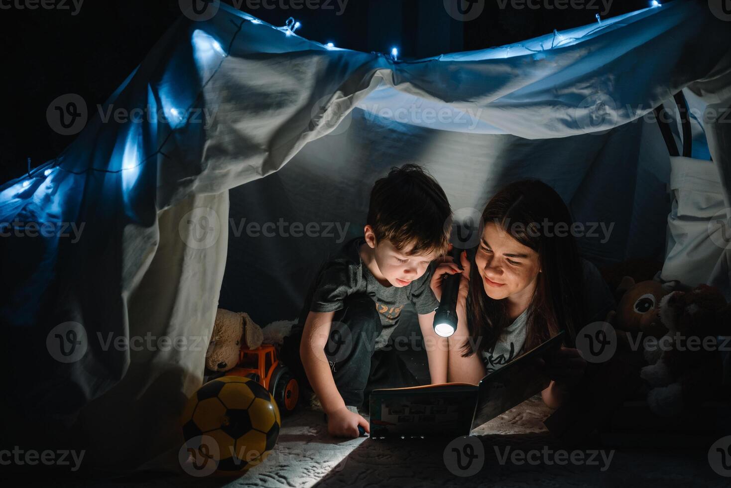 contento familia madre y niño hijo leyendo un libro con un Linterna en un tienda a hogar. familia concepto. foto