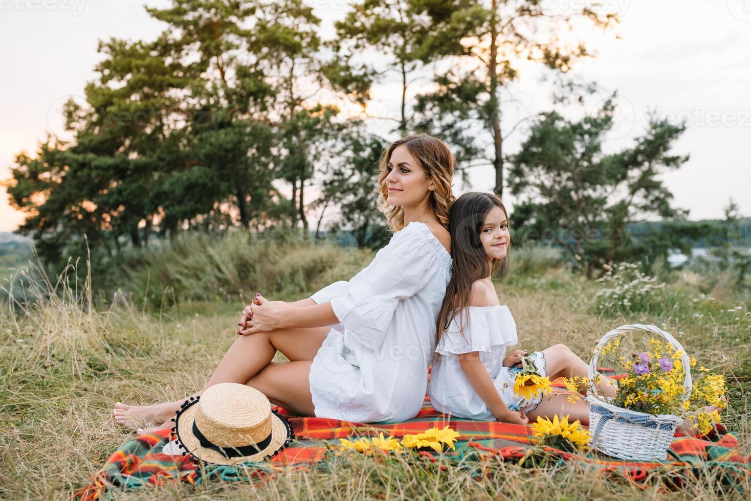 Cheerful mother and her little daughter having fun together in the summer background. Happy family in the nature background. Cute girls with colorful flowers. photo