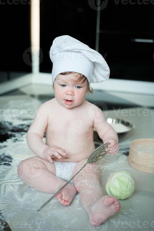 Little boy sitting on carpet in kitchen playing with cooking pots. Cute boy cooking in kitchen at home photo