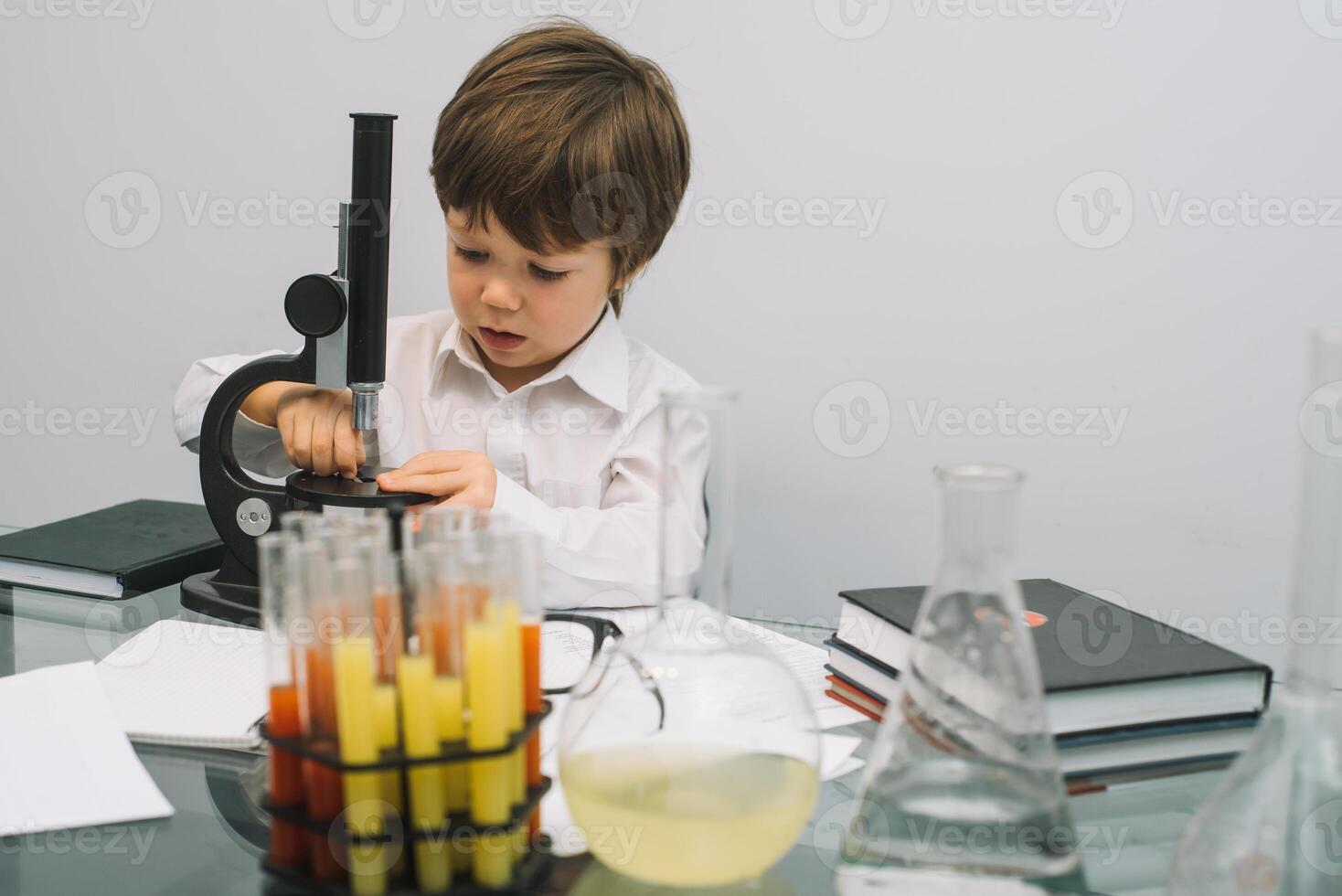 The boy with a microscope and various colorful flasks on a white background. A boy doing experiments in the laboratory. Explosion in the laboratory. Science and education photo