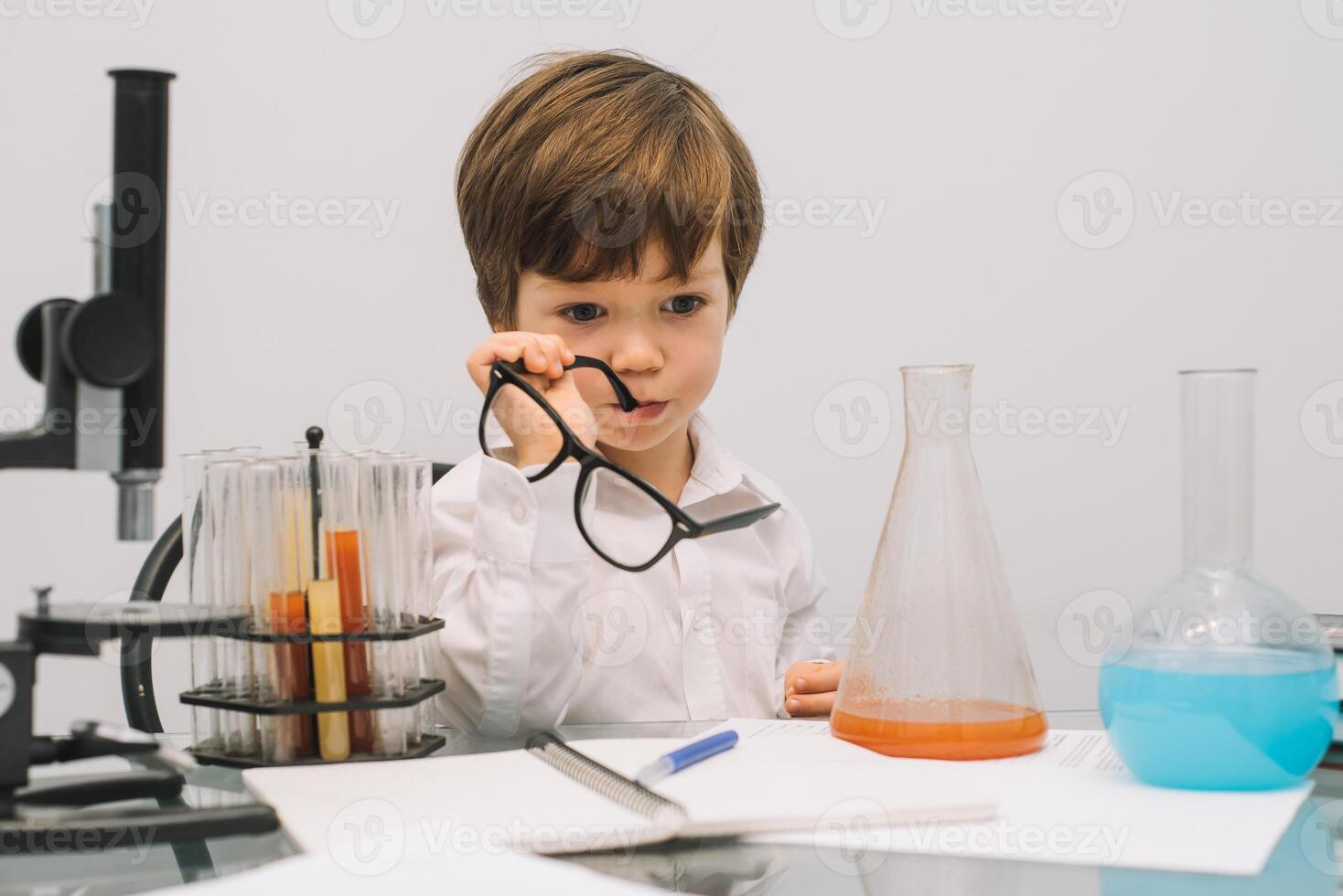 The boy with a microscope and various colorful flasks on a white background. A boy doing experiments in the laboratory. Explosion in the laboratory. Science and education photo
