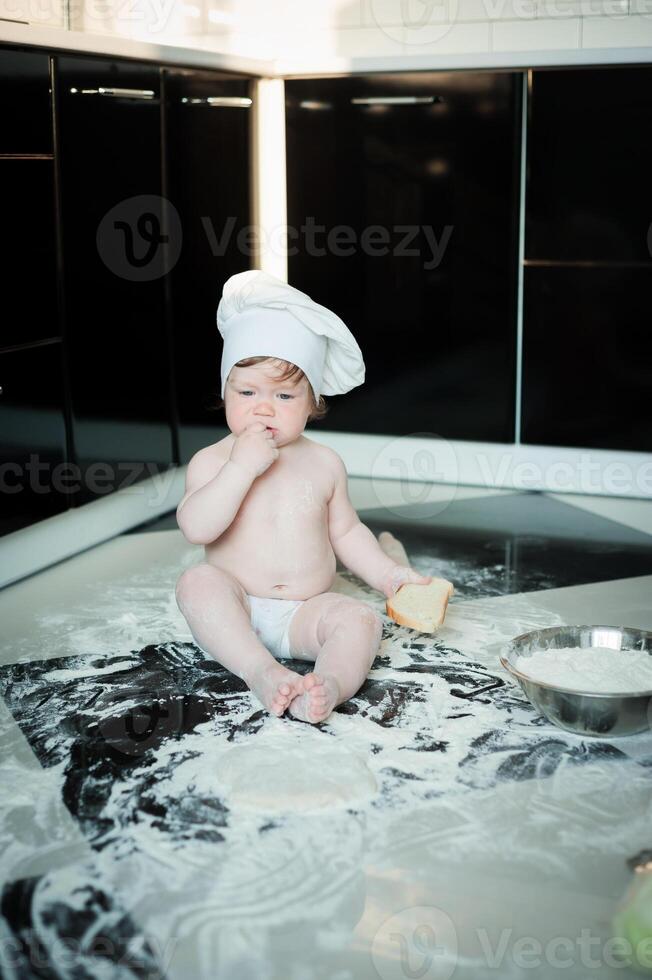 Little boy sitting on carpet in kitchen playing with cooking pots. Cute boy cooking in kitchen at home photo