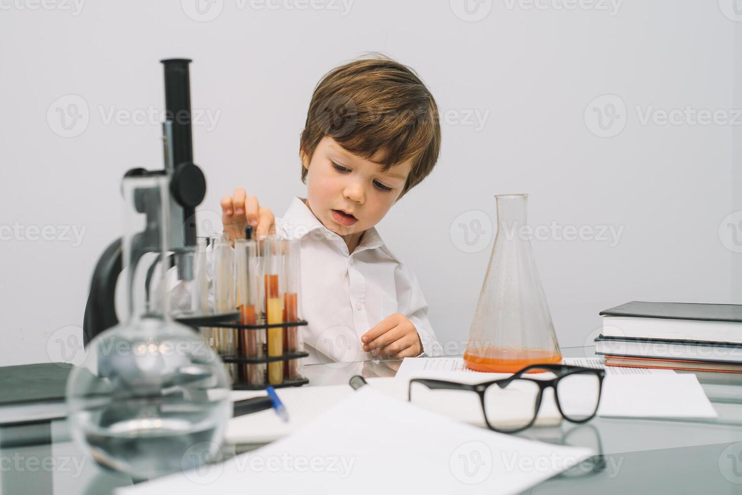 The boy with a microscope and various colorful flasks on a white background. A boy doing experiments in the laboratory. Explosion in the laboratory. Science and education photo