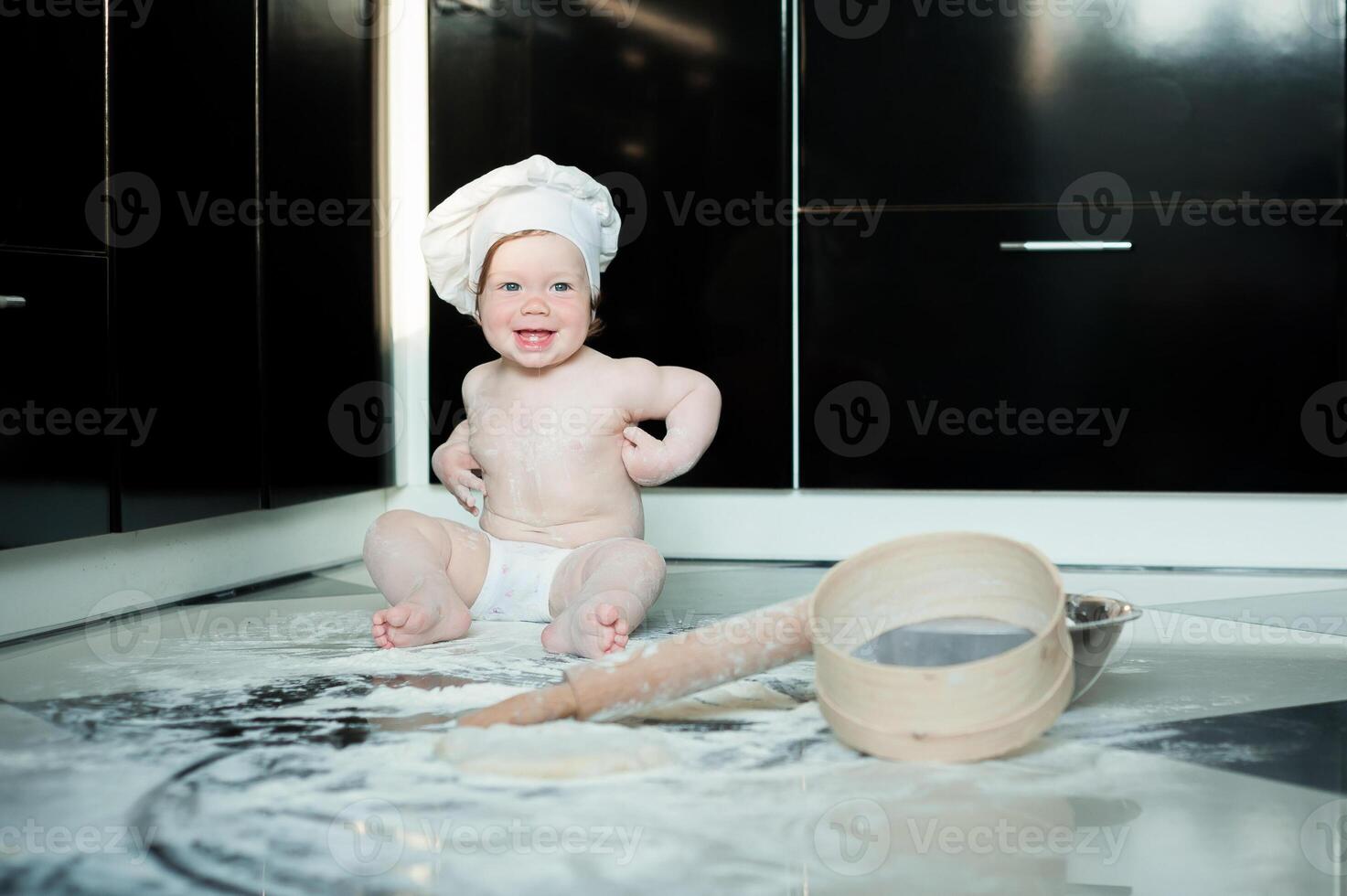 Little boy sitting on carpet in kitchen playing with cooking pots. Cute boy cooking in kitchen at home photo