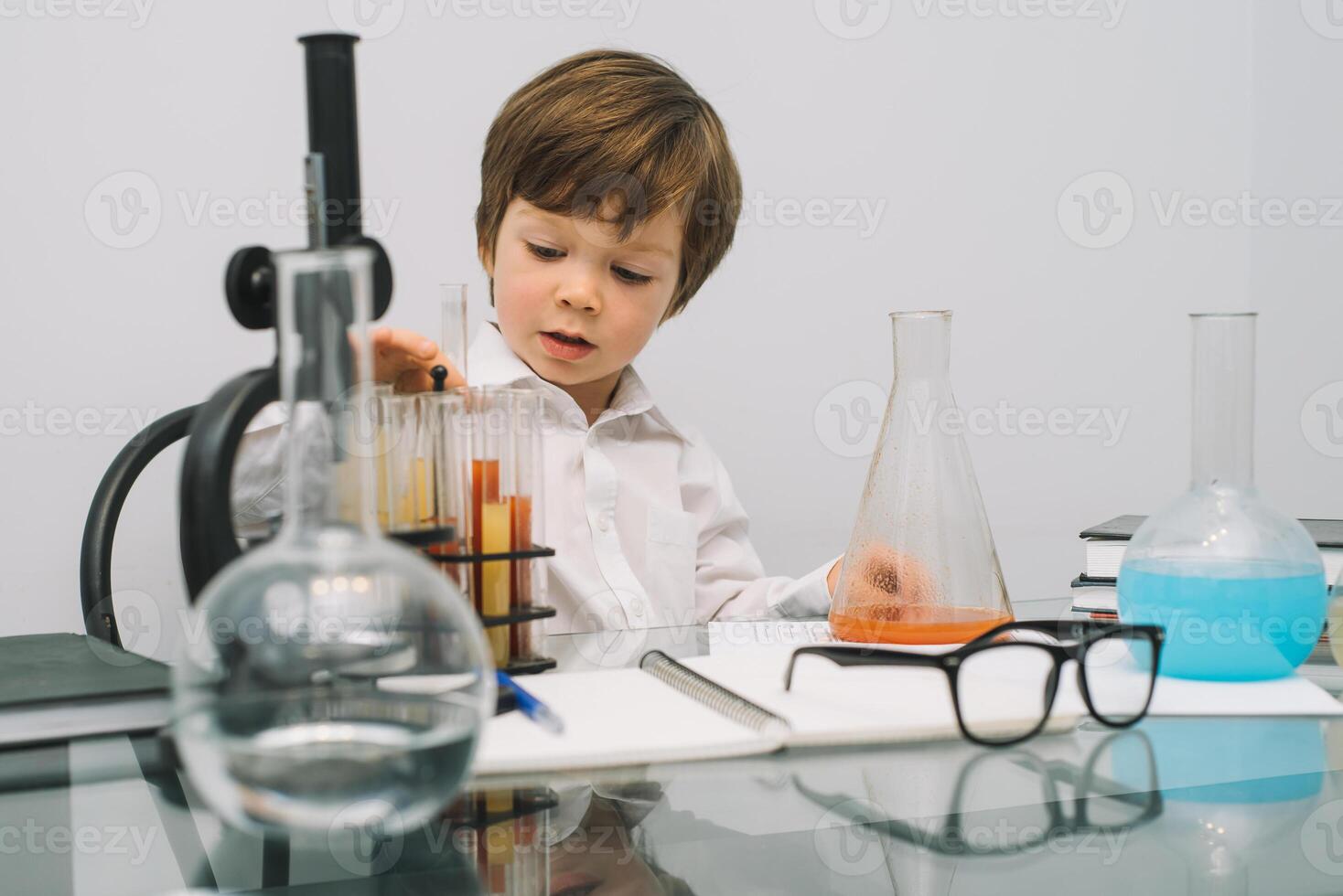 The boy with a microscope and various colorful flasks on a white background. A boy doing experiments in the laboratory. Explosion in the laboratory. Science and education photo