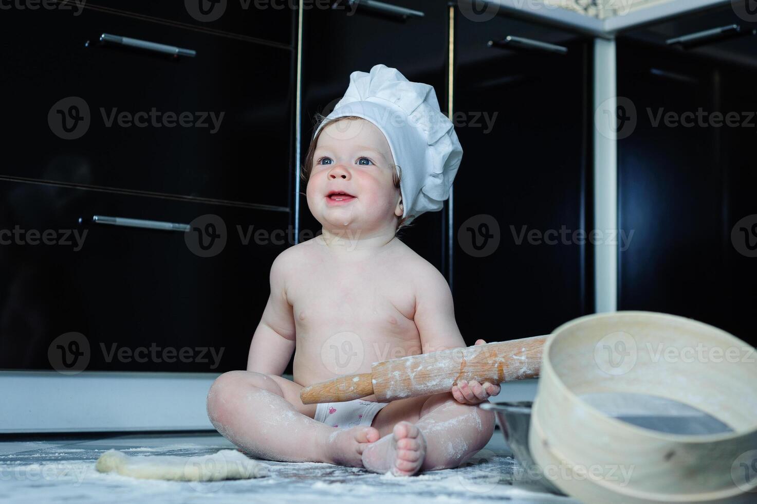 Little boy sitting on carpet in kitchen playing with cooking pots. Cute boy cooking in kitchen at home photo