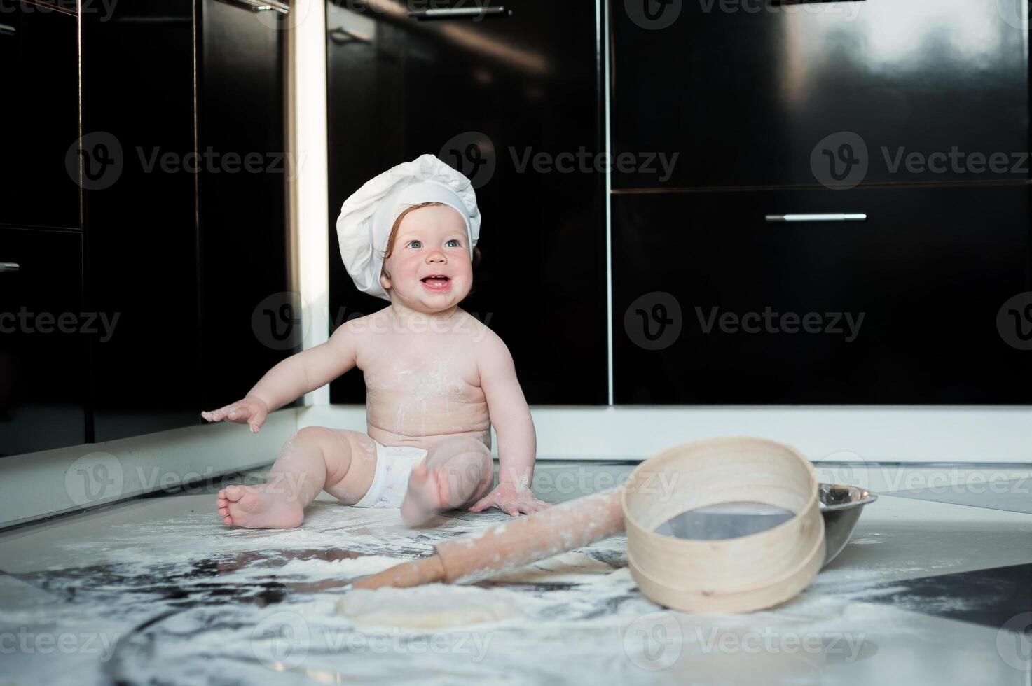 Little boy sitting on carpet in kitchen playing with cooking pots. Cute boy cooking in kitchen at home photo