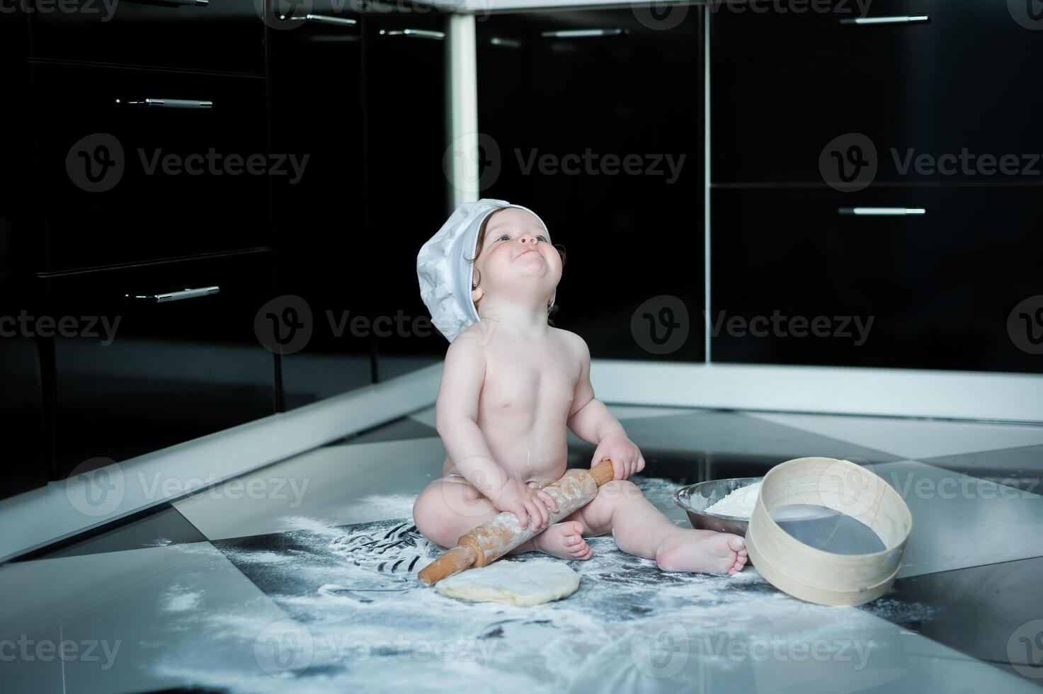 Little boy sitting on carpet in kitchen playing with cooking pots. Cute boy cooking in kitchen at home photo