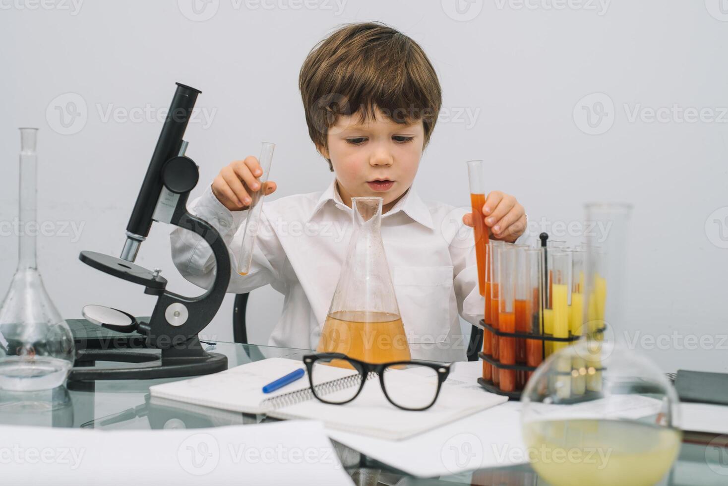 The boy with a microscope and various colorful flasks on a white background. A boy doing experiments in the laboratory. Explosion in the laboratory. Science and education photo
