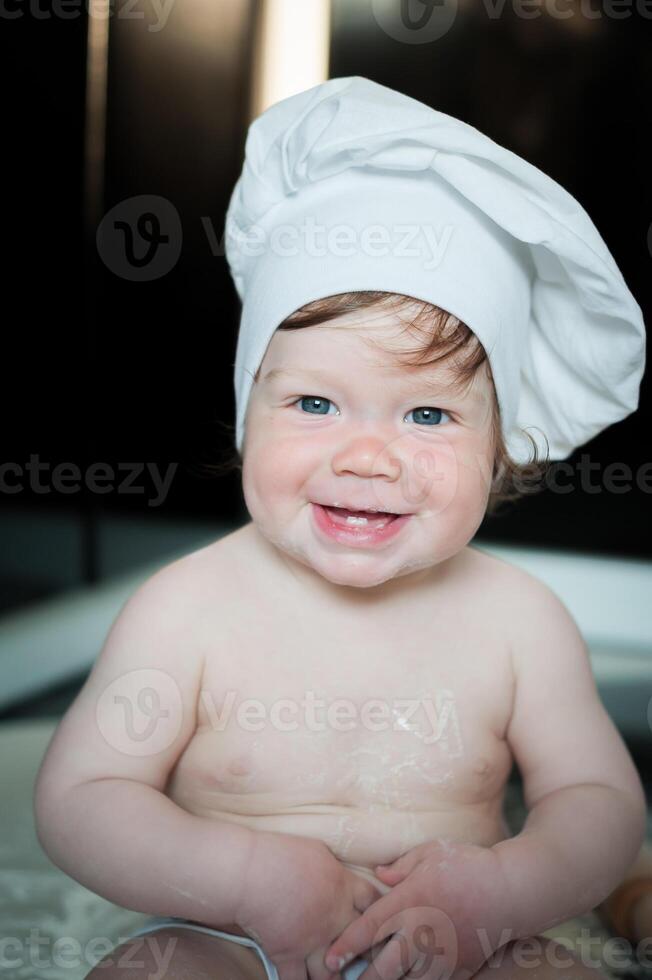 Little boy sitting on carpet in kitchen playing with cooking pots. Cute boy cooking in kitchen at home photo